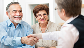 A man and woman shake hands with an older couple, symbolizing a friendly greeting